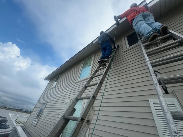 Crew members on ladders working the roofline of a two-story home