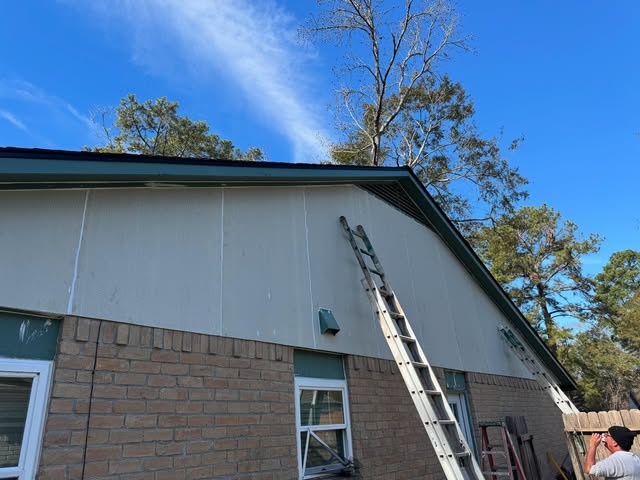 Crew ladder set against a gable during fascia and siding repair on a brick ranch home