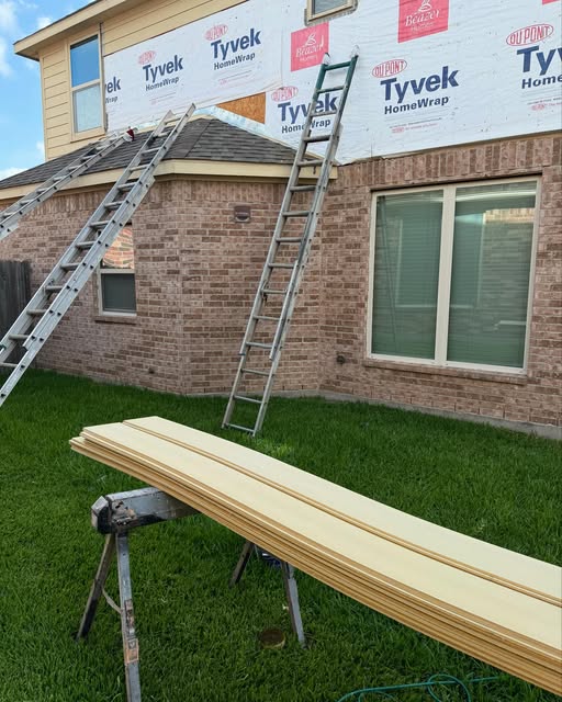 Siding replacement in progress with house wrap installed and primed planks staged on sawhorses