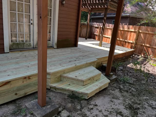 New pressure-treated wood deck and steps built off a back door beside a stained fence